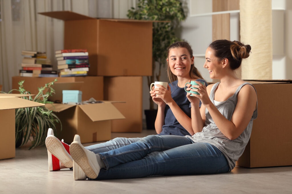 two happy roommates moving home resting and talking sitting on t
